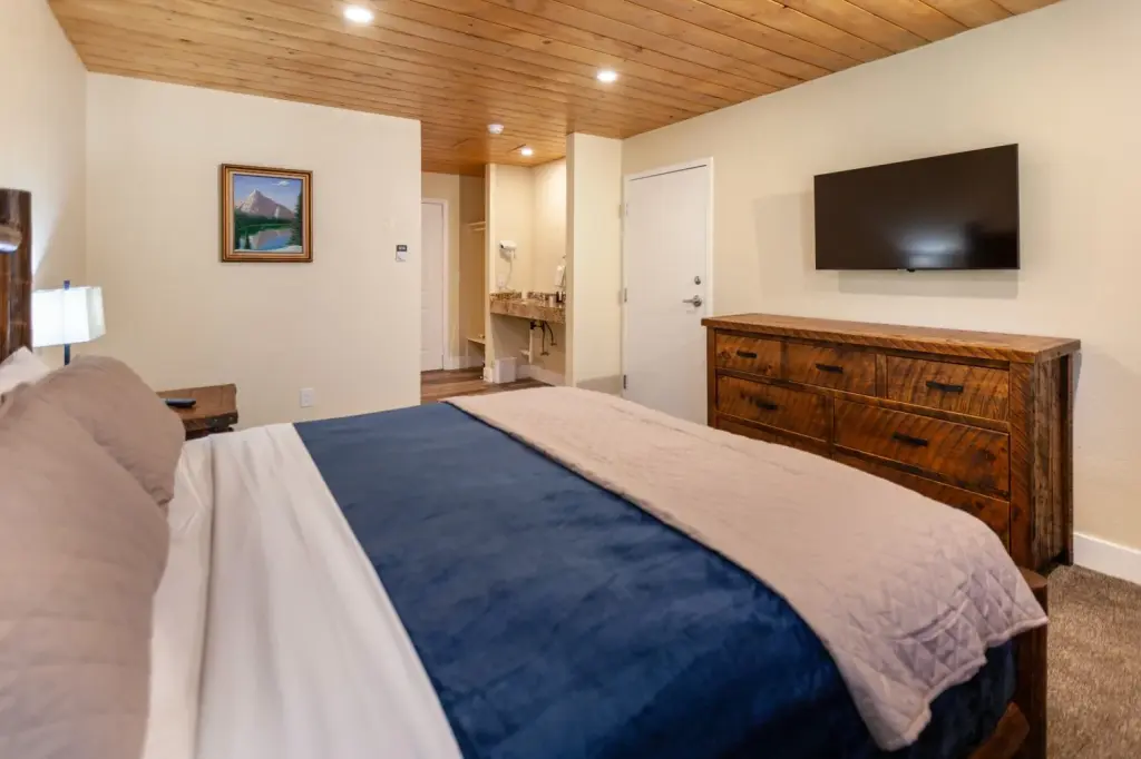 ADA Economy King at Tahquitz Pines Retreat, a king bed with a log headboard facing a wall TV and rustic dresser