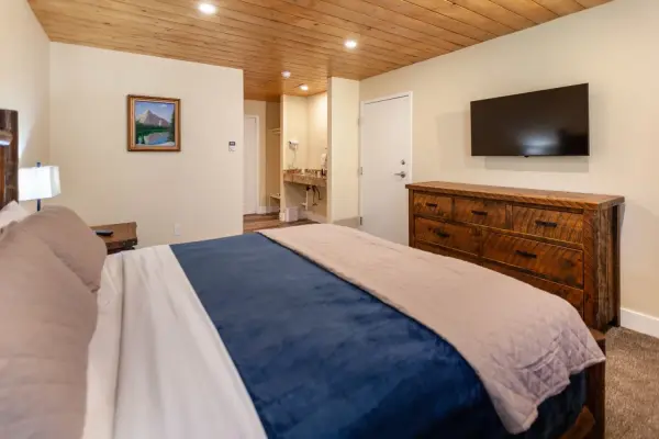 ADA Economy King at Tahquitz Pines Retreat, a king bed with a log headboard facing a wall TV and rustic dresser