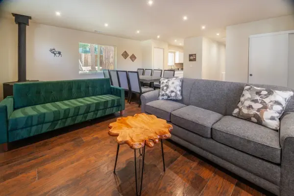 Cottage #74 at Tahquitz Pines Retreat, a green velvet sofa and gray sofa before a long dining table and wood stove