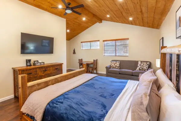 King Cabin at Tahquitz Pines Retreat, a king bed facing a sofa and small dining table under a vaulted pine ceiling