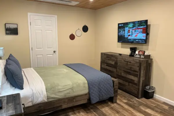 Lower Bridal Interior Room at Tahquitz Pines Retreat, a bed with a green blanket facing a rustic dresser and wall TV