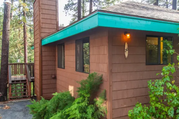 New Rustic Suite at Idyllwild Inn, a wood-sided cabin with teal eaves, a lit porch lamp and stairs up to a side deck