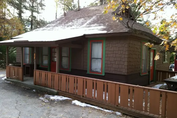 Rustic Cabin, 3 Bedroom at Idyllwild Inn, a shingled cabin with red doors, green trim and a wooden railing, snow on the roof