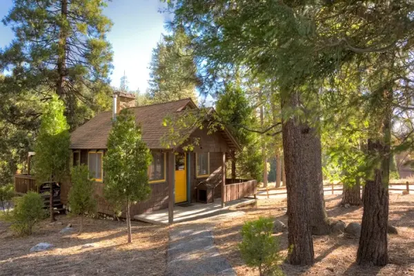 Rustic Studio at Idyllwild Inn, a brown wood cabin with yellow-trimmed windows and a small porch among tall pines
