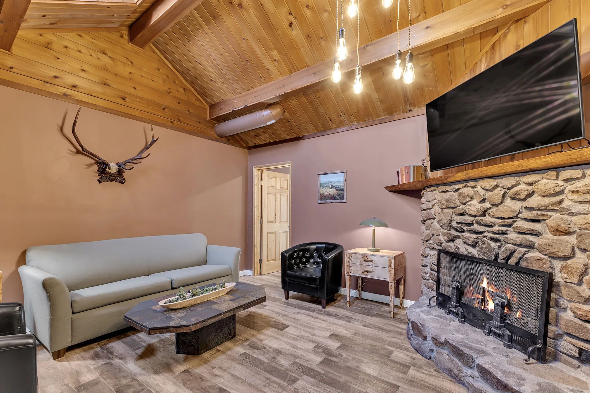 A suite living room with a river-rock fireplace, a sofa and leather armchair, and a wood-beamed ceiling