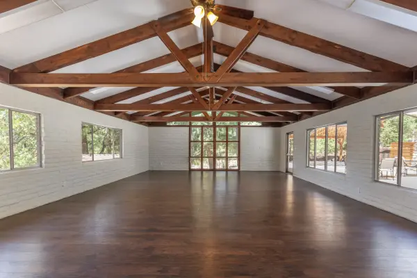 The open interior of Altitude Hall, with white walls, a timber-truss ceiling, wood floors and windows onto the pines