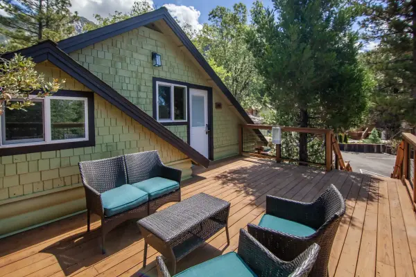 Wicker seating with teal cushions on the sunny wooden deck of a green cabin at Tahquitz Pines Retreat
