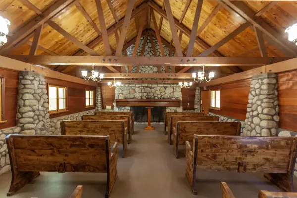 The center aisle of the chapel at Tahquitz Pines Retreat, wooden pews leading to a stone fireplace under a pine ceiling