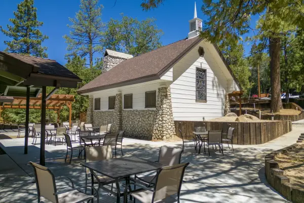 The white chapel at Tahquitz Pines Retreat with its steeple and river-rock walls, patio tables in the sun beside it