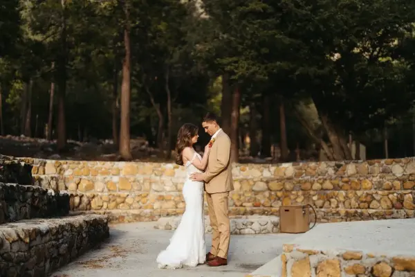 A bride and groom embracing on the stage of the stone amphitheater at Tahquitz Pines Retreat, pines rising behind the curved stone tiers