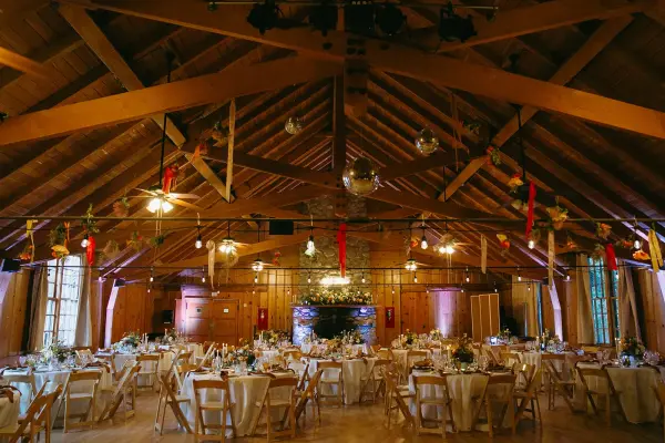 A timber-beamed hall at Tahquitz Pines Retreat set for a wedding reception, round tables in white linen, garlands overhead and flowers on the stone fireplace