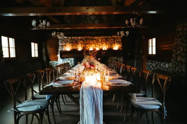 A candlelit long table with flowers and cross-back chairs in a river-rock-walled room at Tahquitz Pines Retreat