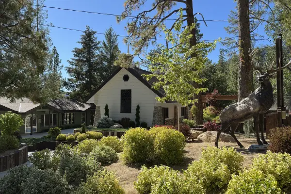 The white chapel at Tahquitz Pines Retreat among the pines, with a bronze elk statue in the garden in front